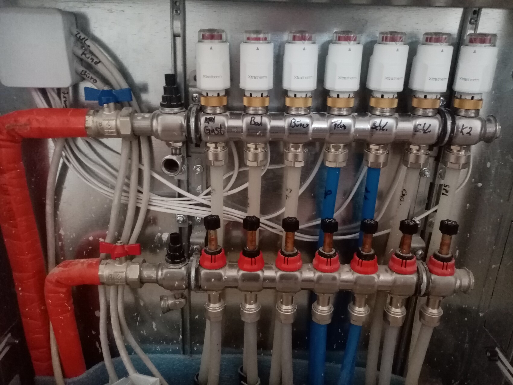 Heizungsverteiler mit acht Absperrventilen, Thermostatköpfen und roten/blauen Zuleitungen.
