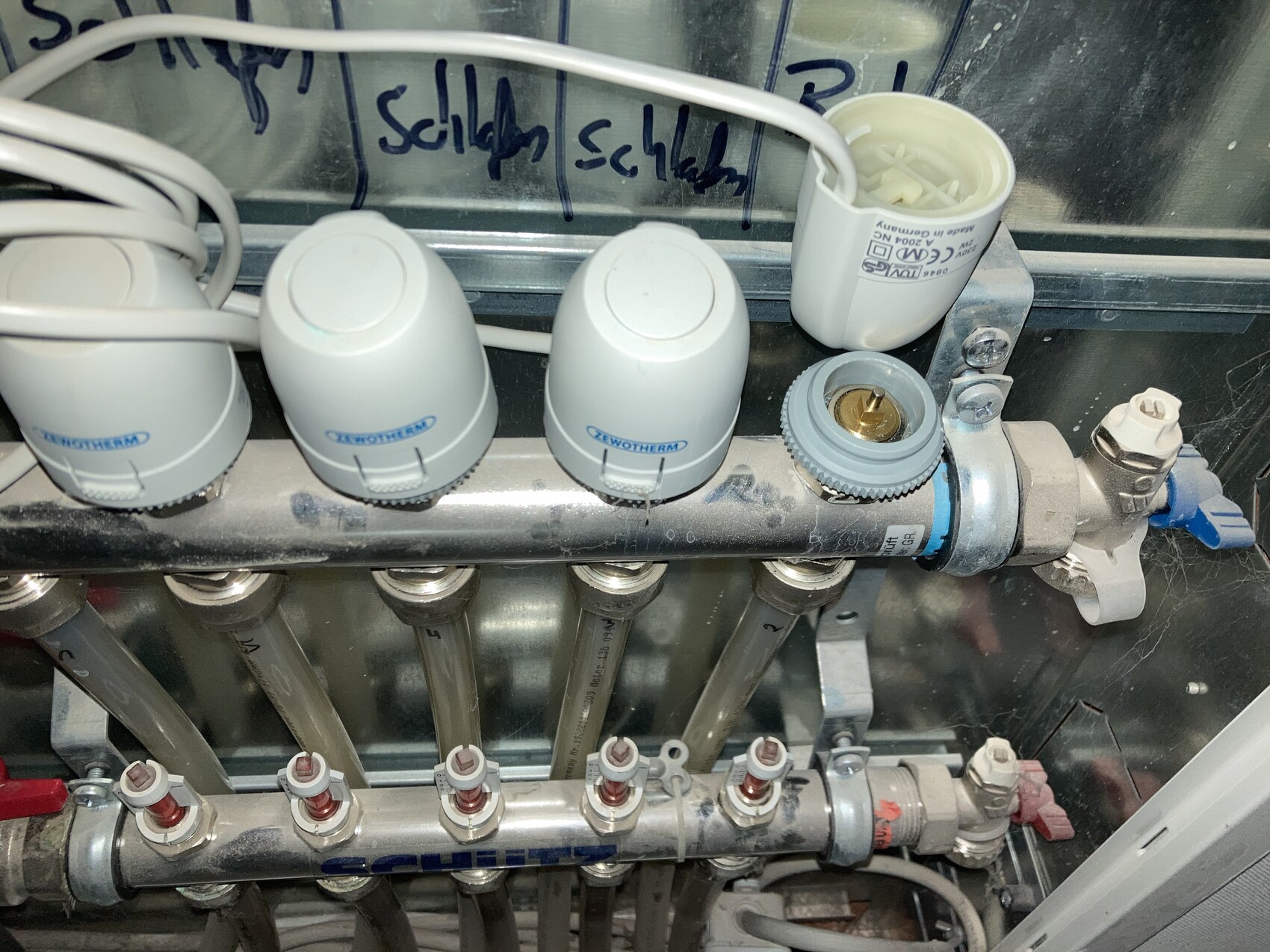 Verteiler mit drei grauen Thermostat-Knöpfen, Rohrleitungen und Ventilen in einer Sanitäranlage.