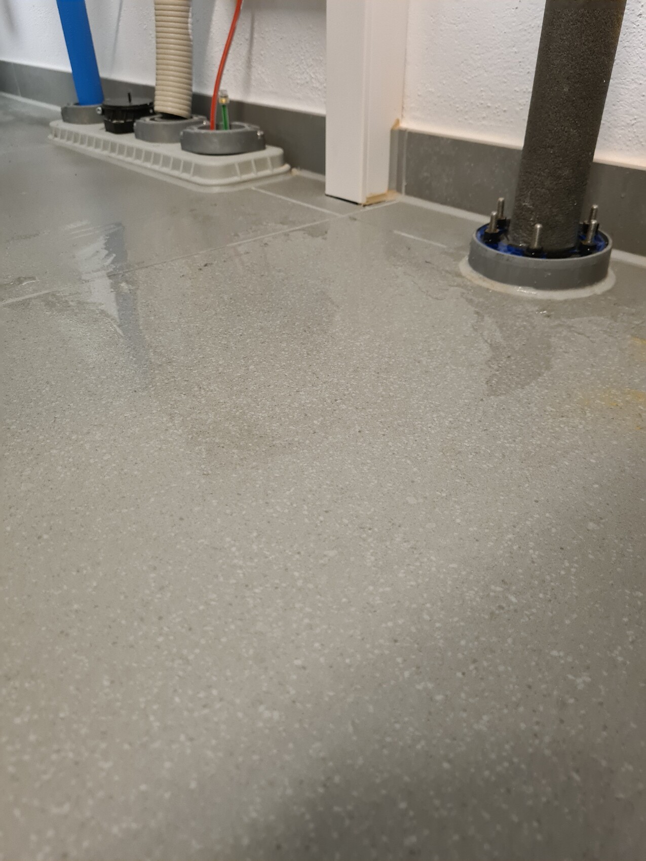 Grau gepunkteter Epoxidboden in einer Werkstatt; Rohre und Stützpfosten sichtbar.