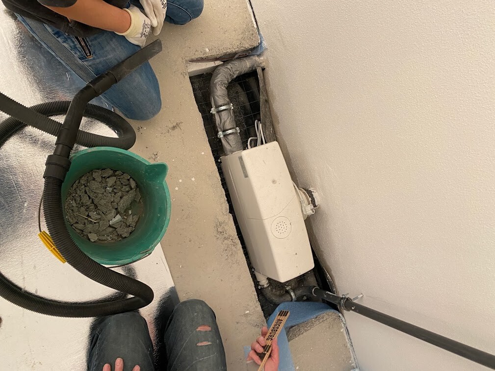 Baustelle: Haustechnik-Installation hinter Wand, Rohre, Verteilereinheit; Eimer mit Kies.