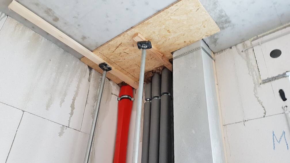 Rohbau-Innenraum mit roten und grauen Rohren, Holzplatte und Metallstützen.