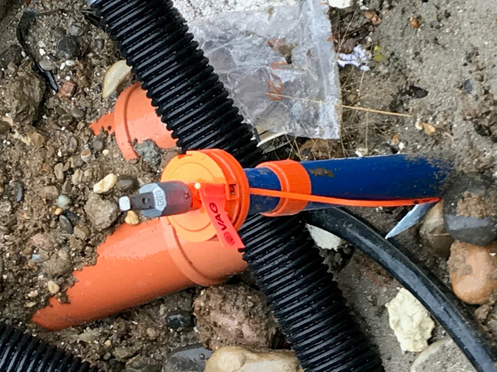 Baustelle mit orange Rohrleitungen, schwarzem Kabelschlauch und Kies