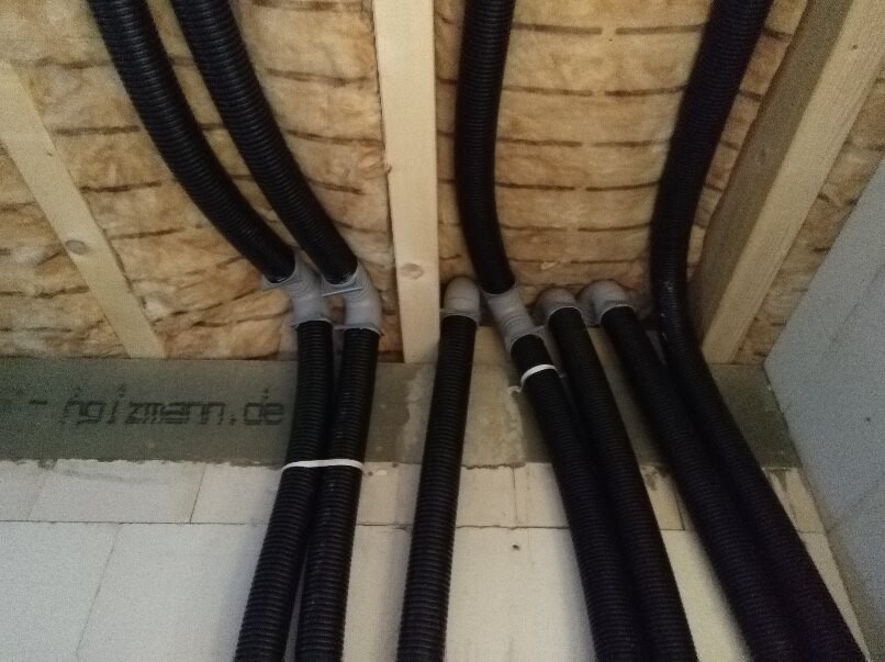 Mehrere schwarze Kabelschläuche verlaufen von der Decke nach unten, verbunden mit grauen Klemmen.