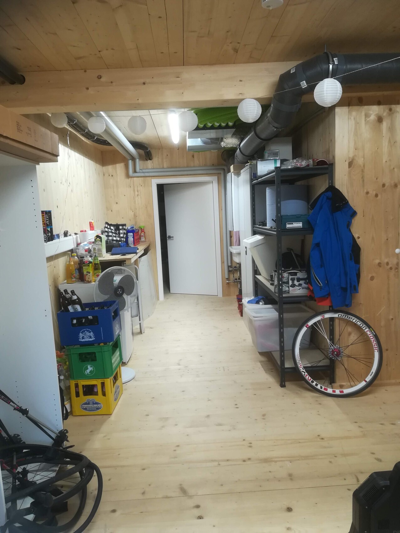 Holzverkleideter Keller-Werkraum mit Regalen, Fahrradrad, Jacke und Getränkekisten.