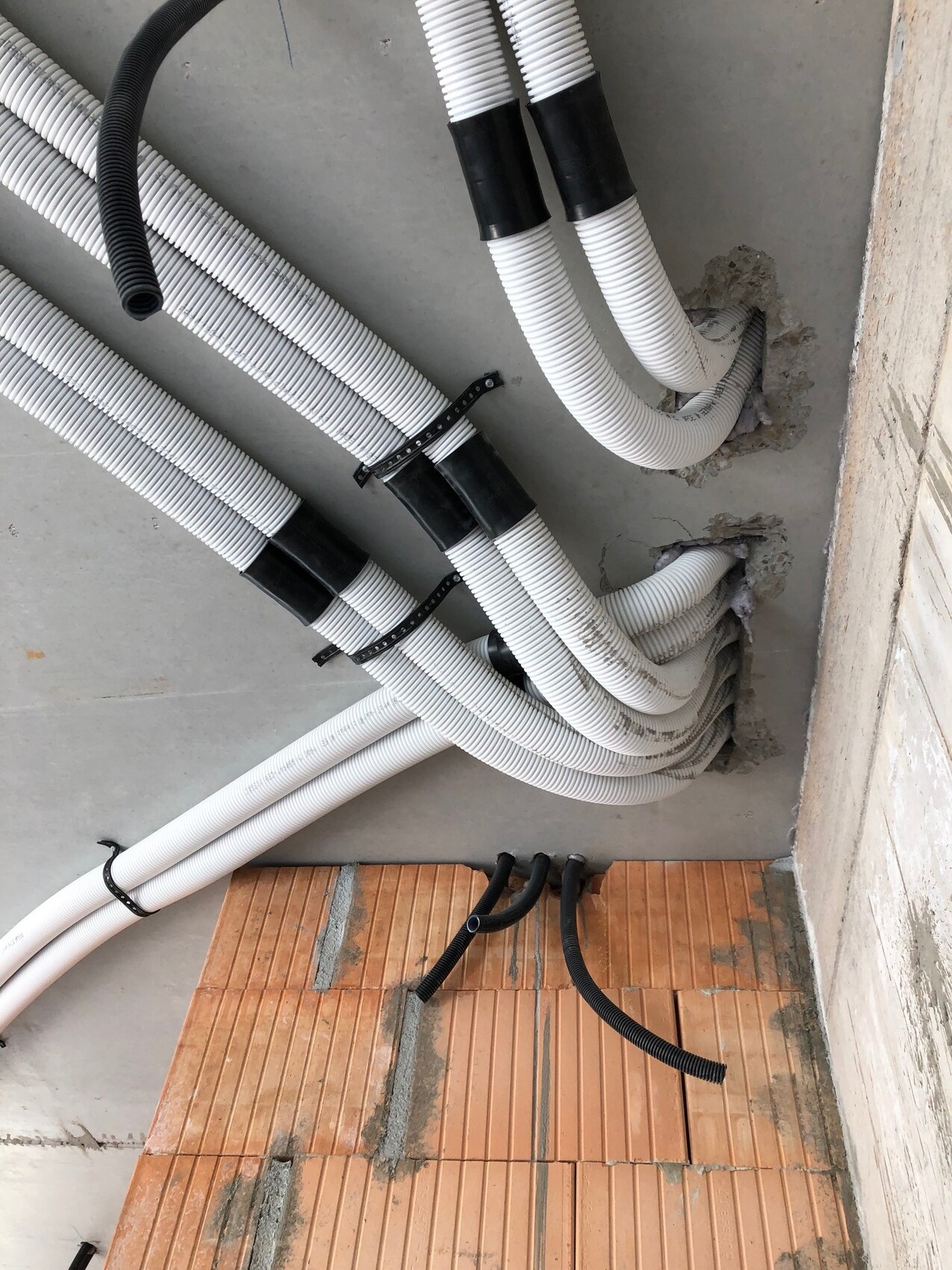 Weiße flexible Rohre und schwarze Kabelschläuche im Rohbau, Haustechnik-Installation