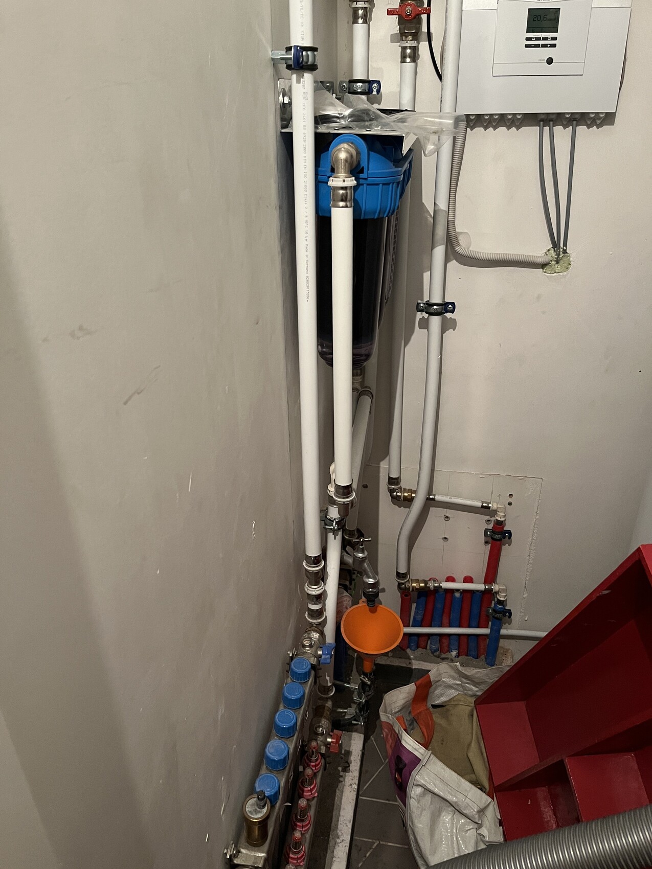 Kleiner Technikraum mit Wasserfilter: blaues Filtergehäuse, Rohre, Ventile, Messgerät.