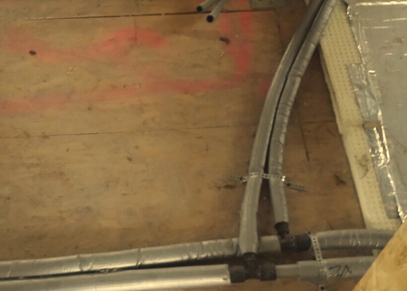 Holzfußboden mit installierten Metallrohren, flexiblen Kabelkanälen und Metallclips.