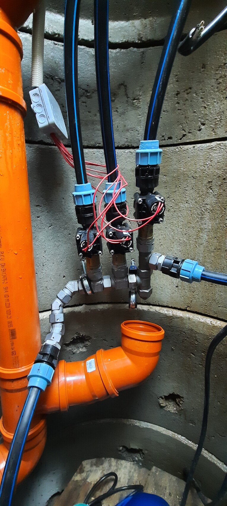 Mehrfaches Rohrsystem mit blauen Kupplungen, Ventilen, roten Drähten und orange Rohren.