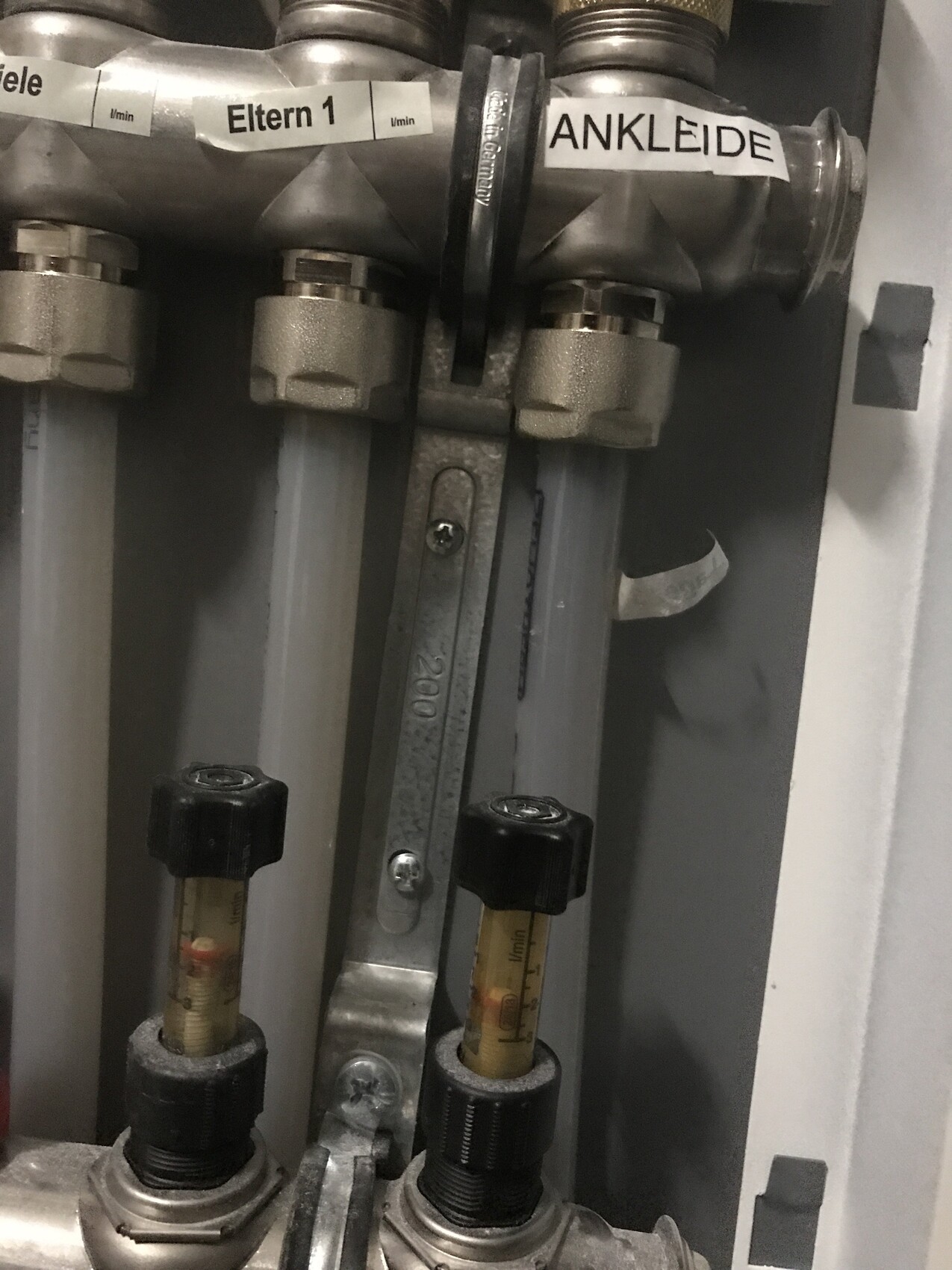 Nahaufnahme eines Rohrsystems mit zwei Messröhren und Etiketten 'Eltern 1' und 'ANKLEIDE'.