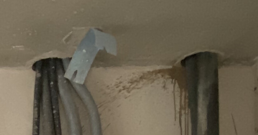 Zwei Rohre an feuchter Wand; braune Wasserflecken unterhalb der Decke, Klebeband sichtbar.