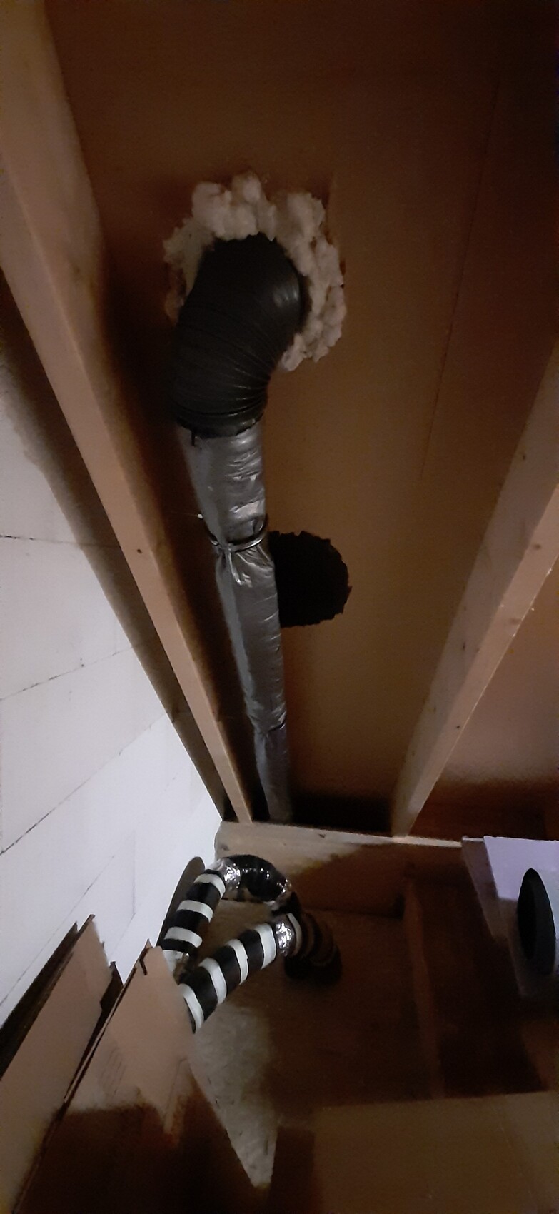 Isoliertes Rohr durch Loch in Holzdecke, schwarzer Flexschlauch und Schaumdämmung.