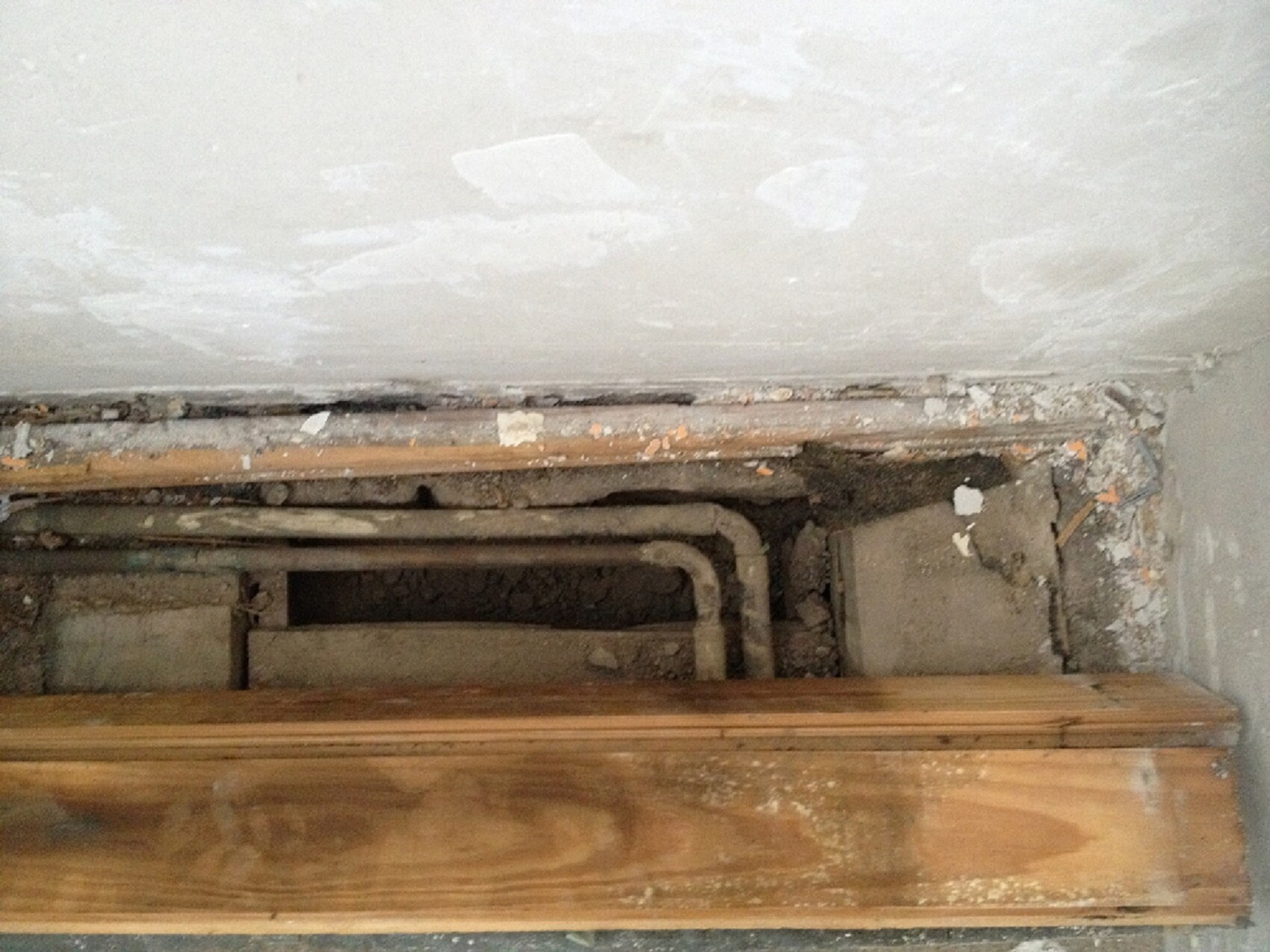 Kellerbereich mit sichtbaren Rohren und Putzresten hinter einer Holzverkleidung