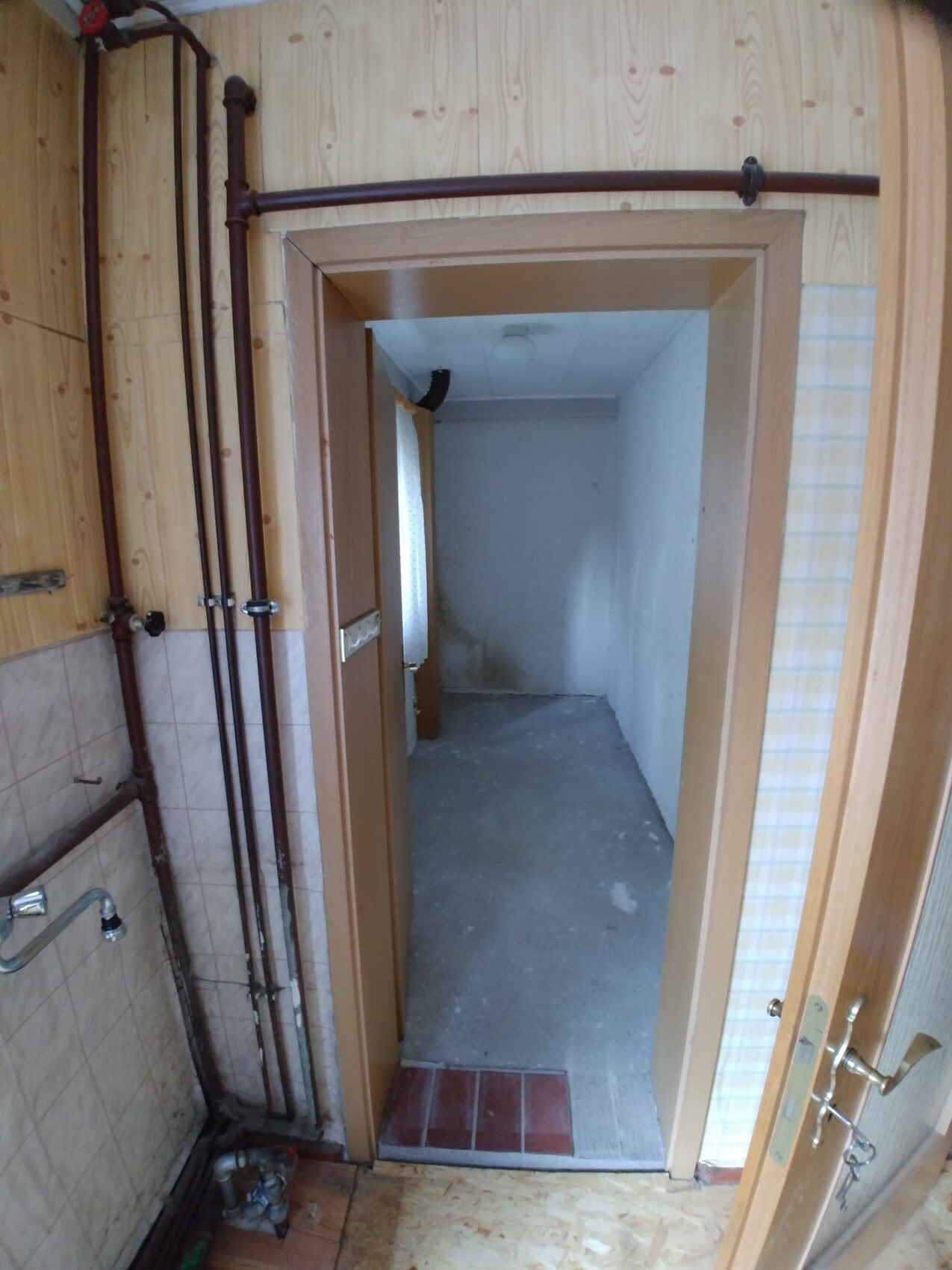 Unfertiger Innenraum mit sichtbaren Kupferrohren an der Wand und offener Holztür
