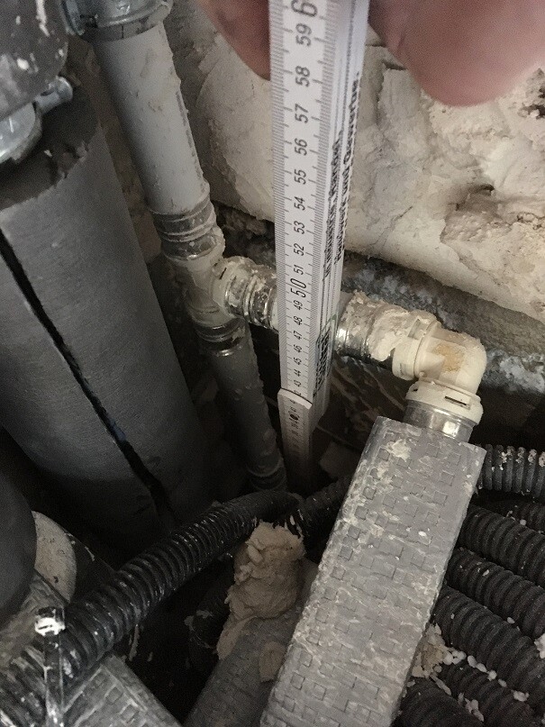 Blick auf Rohrleitungen, Messband und Dämmung hinter Wand im Baubereich