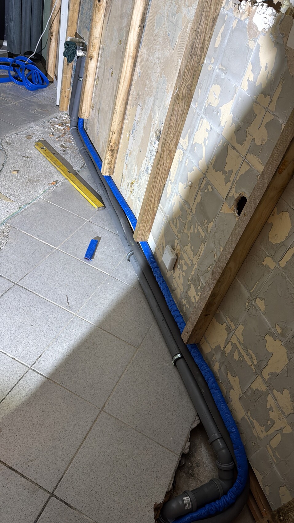 Rohrleitungen und Dämmung verlaufen an einer Wand bei Renovierung, Fliesenboden sichtbar.