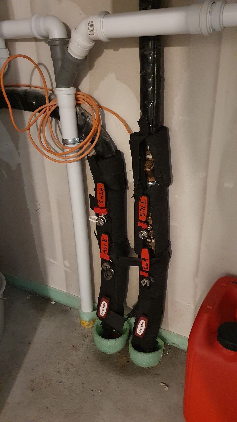Installationsbereich im Keller mit Rohrleitungen, Isolierung, Ventilen und Kabeln