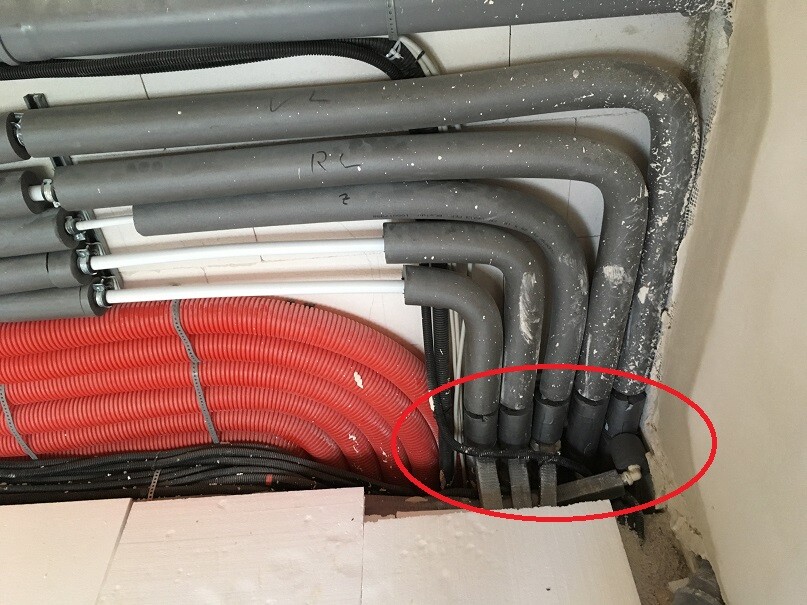 Mehrere graue Rohre und rotes Kabel, rechts unten Rohrschelle.