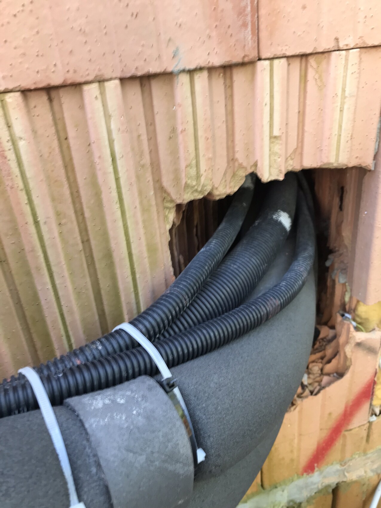 Offene Bruchstelle in der Ziegelwand; schwarze flexible Leitungen, mit Kabelbindern befestigt.