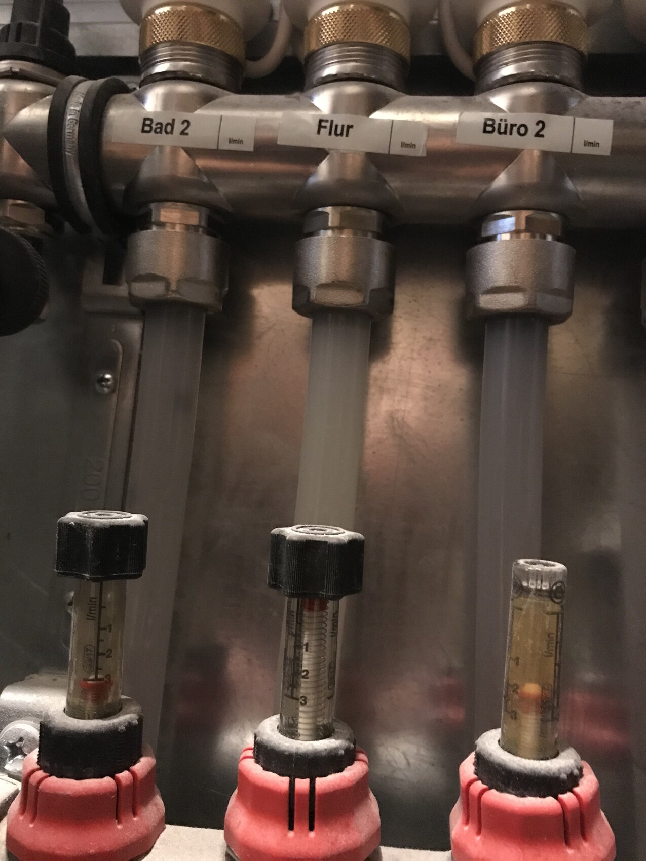 Drei Glasröhrchen mit Skalen an einer Metallrohrleitung; Beschriftung Bad 2, Flur, Büro 2