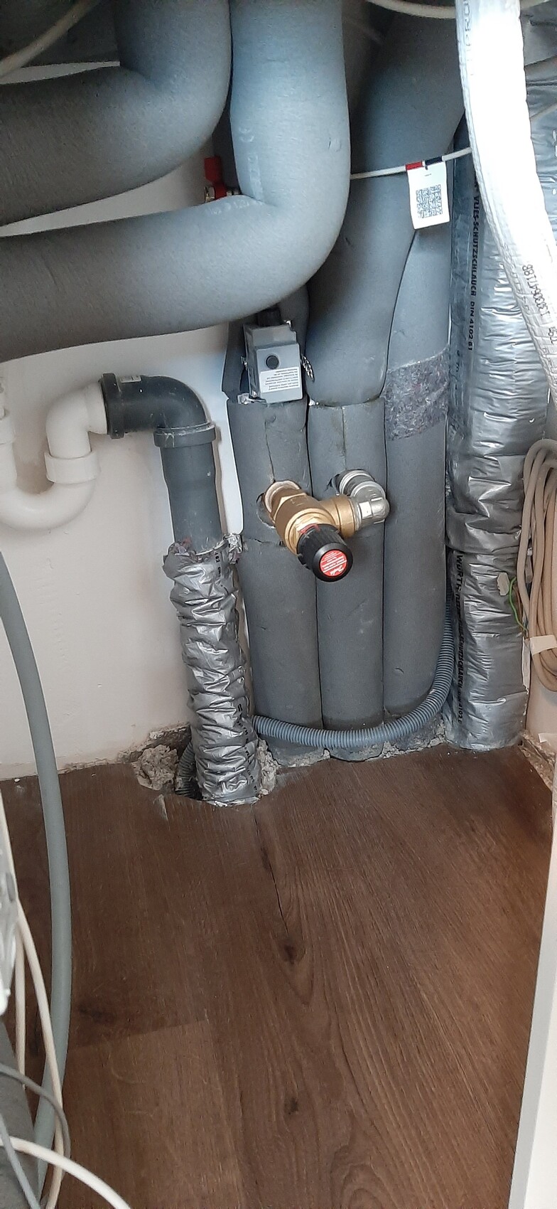 Unterbau: isolierte Rohre, Absperrventil, PVC-Siphon, flexibles Rohr, Holzboden.