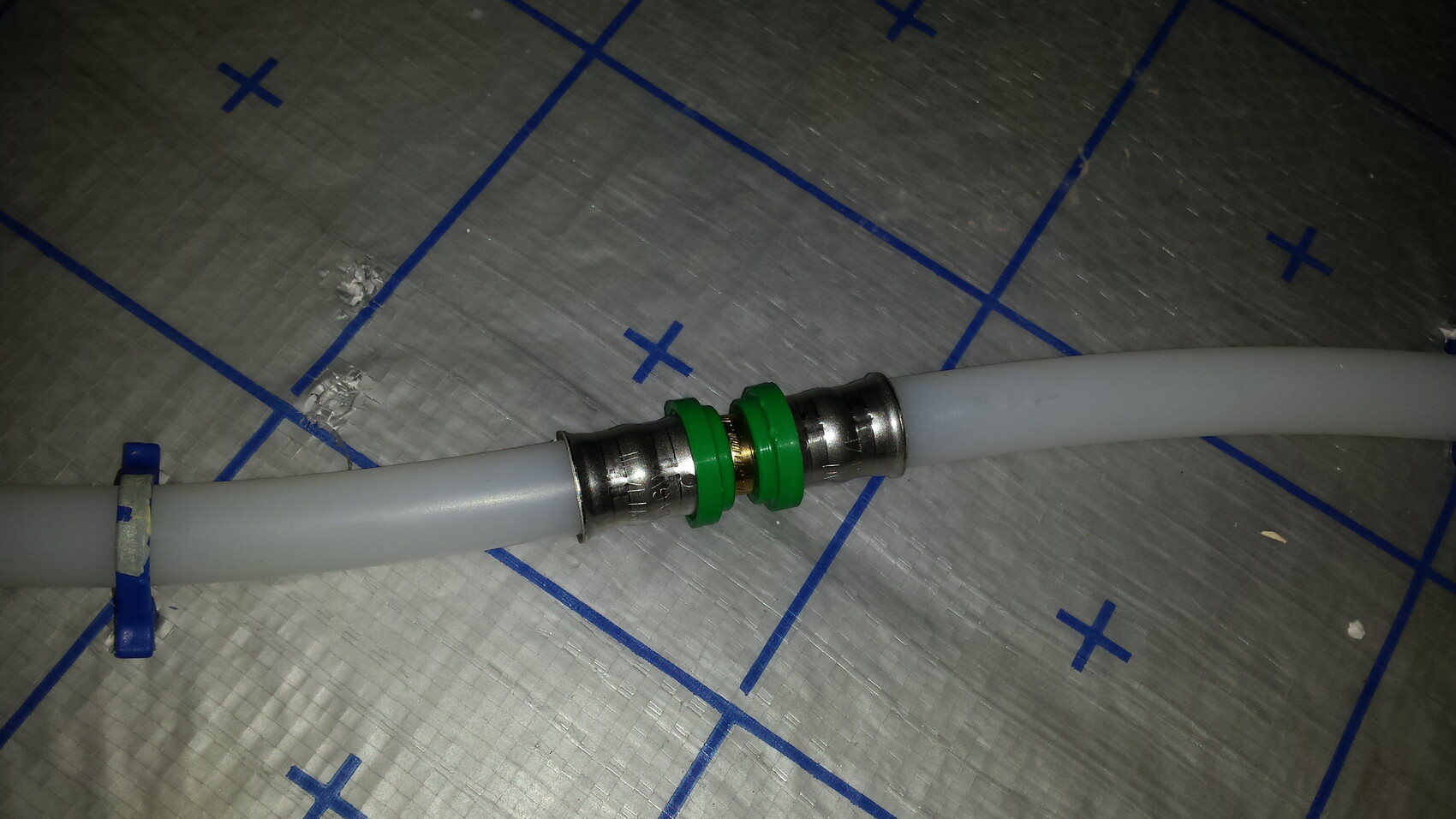 Grau PVC-Schlauch mit silberner Rohrverbindung und grünen Dichtringen auf Baufolie.