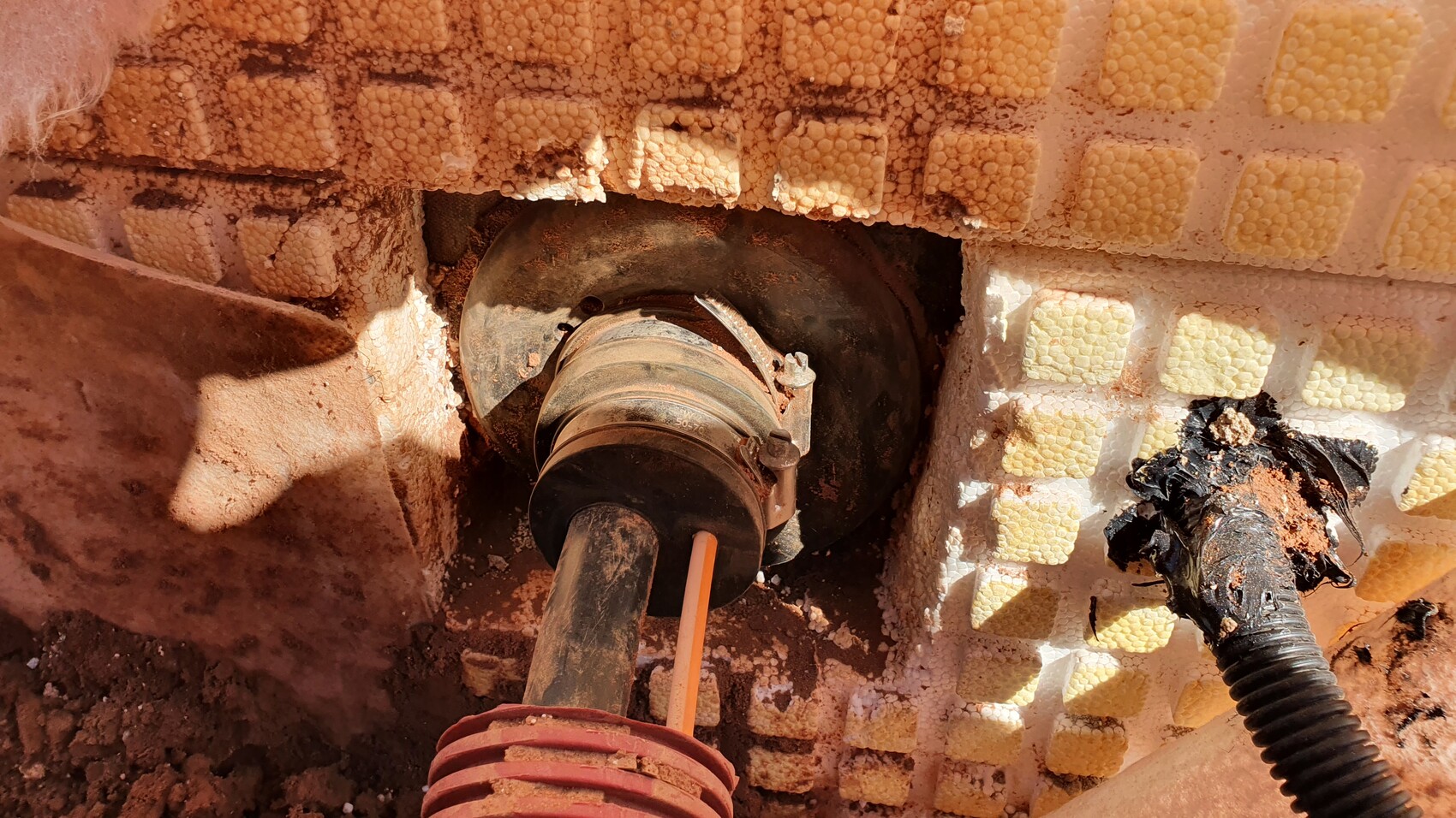 Rundes Rohrstück in Wand aus gelben Styroporblöcken; Schlauch und Dreck daneben.