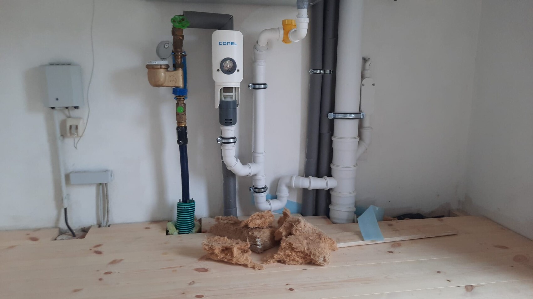 Sanitärinstallation mit PVC-Rohren, CONEL-Filter, Baustoffreste auf Holzboden.