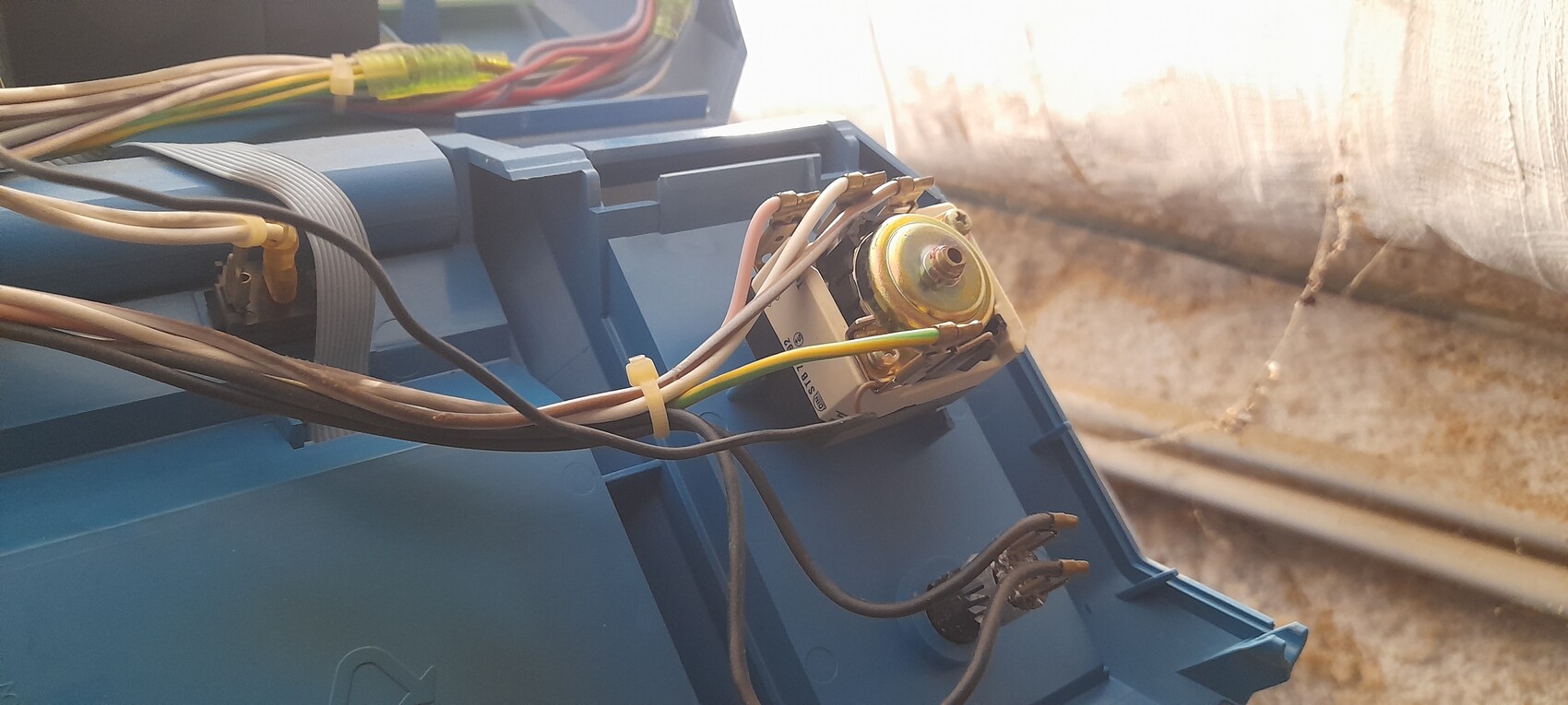 Nahaufnahme einer blauen Elektronikbox mit Kabeln; rundes Metallbauteil mit Anschlüssen.