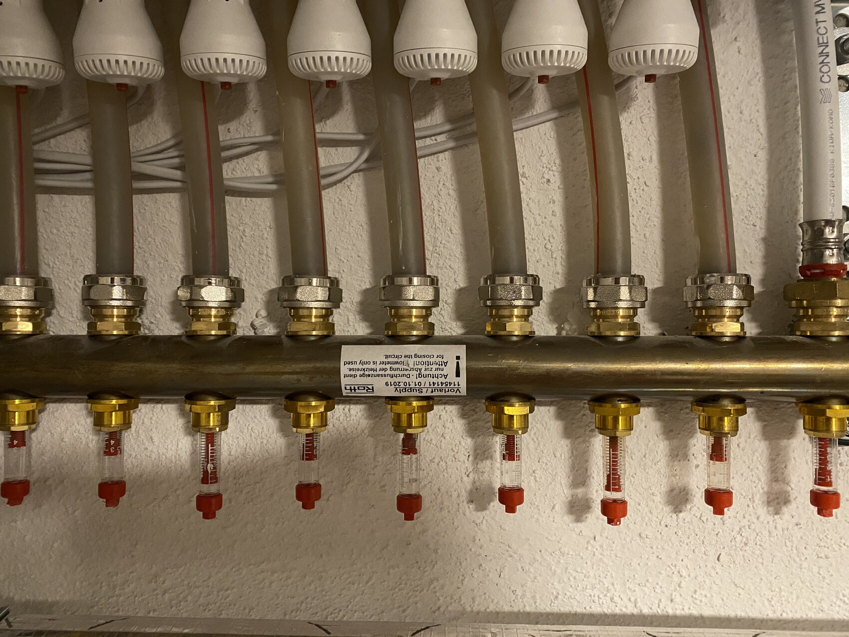 Verteilerleiste einer Heizungsanlage mit Ventilen und Durchflussmessern.