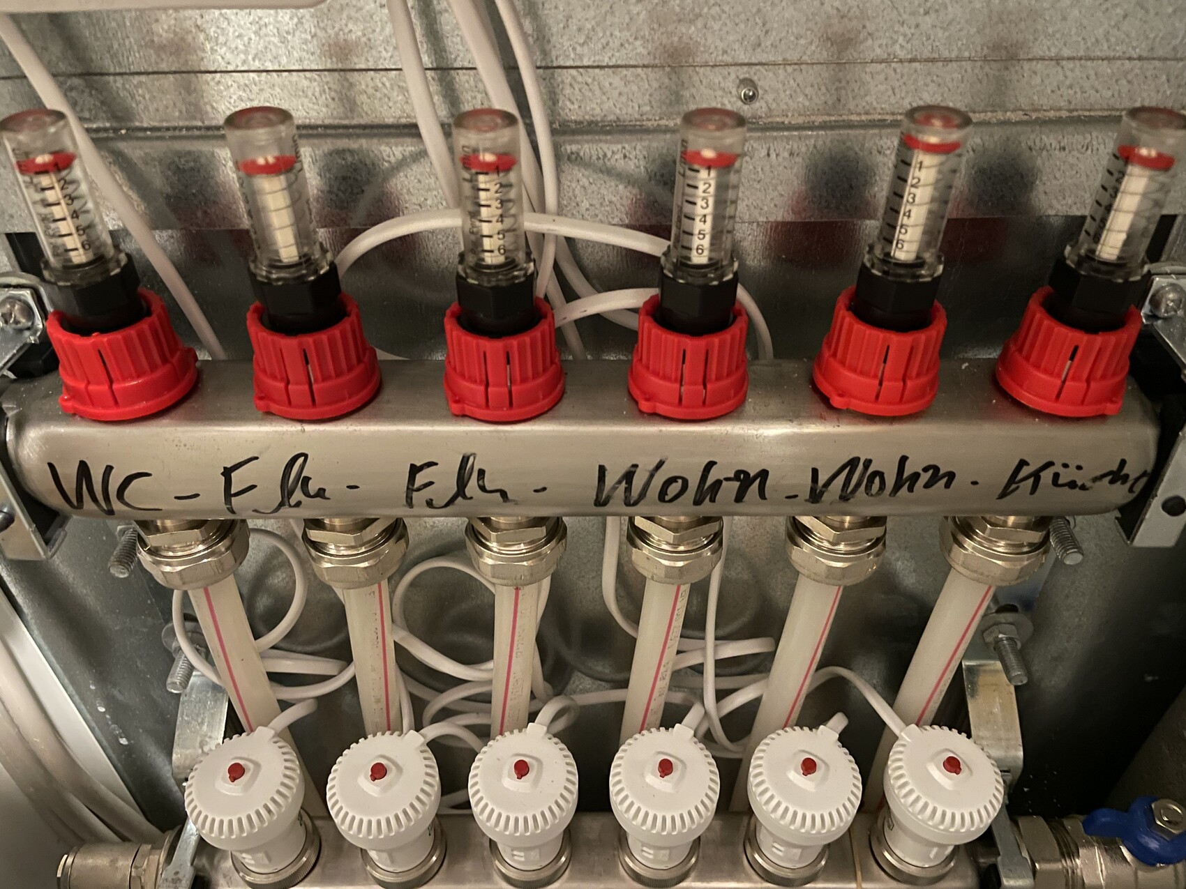 Mehrere Durchflussmesser mit roten Skalenkappen und weißen Schläuchen auf einer Metallleiste.