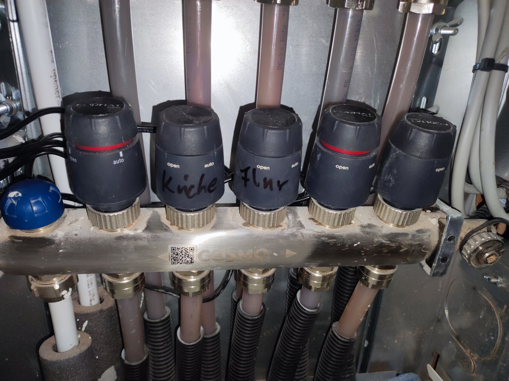 Fünf schwarze Drehknöpfe mit rotem Ring an einem Metallblock, Schläuche dahinter.