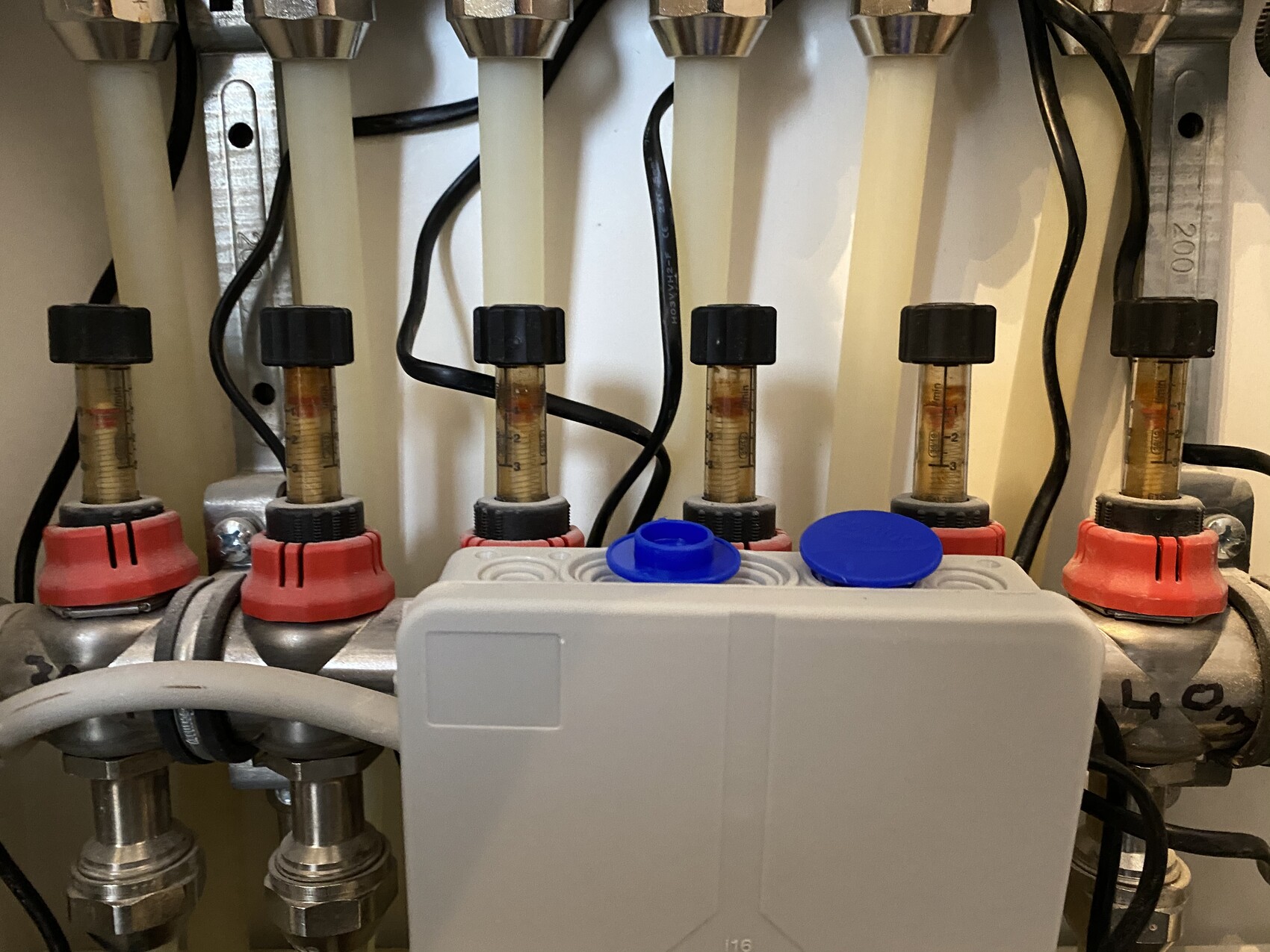 Verteilersystem in Heizungsanlage mit Durchflussmessern, rotem Ventilgriff und Steuereinheit.