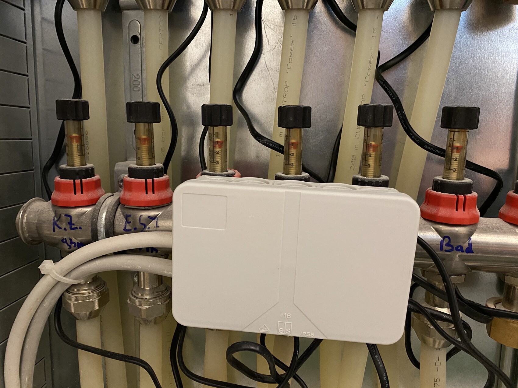 Nahaufnahme eines Heizungsverteilers mit mehreren Absperrventilen, Schläuchen und einer weißen Box.