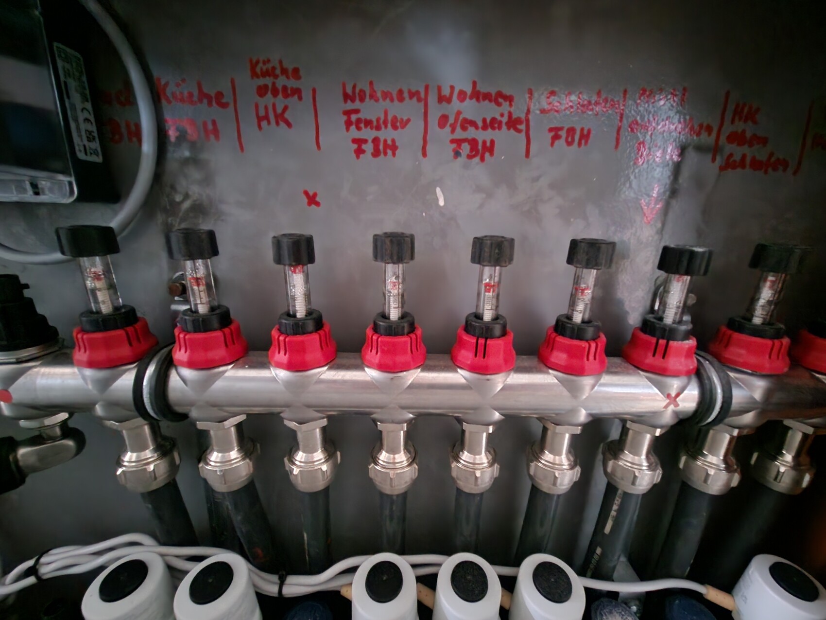 Verteilerleiste mit roten Griffventilen und Schläuchen in Haustechnik