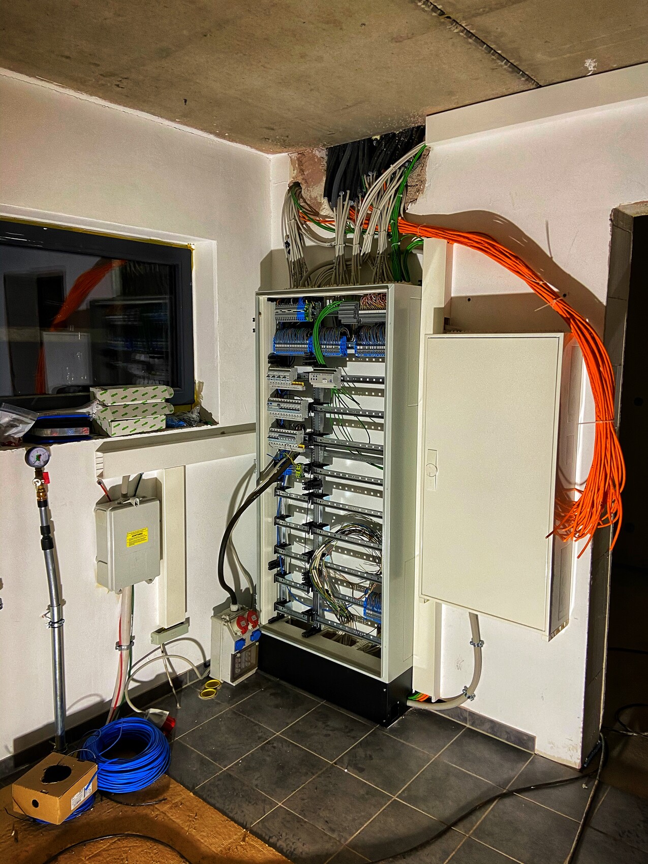 Offener Serverschrank mit vielen blauen, grünen und orangen Kabeln; links Werkzeuge.
