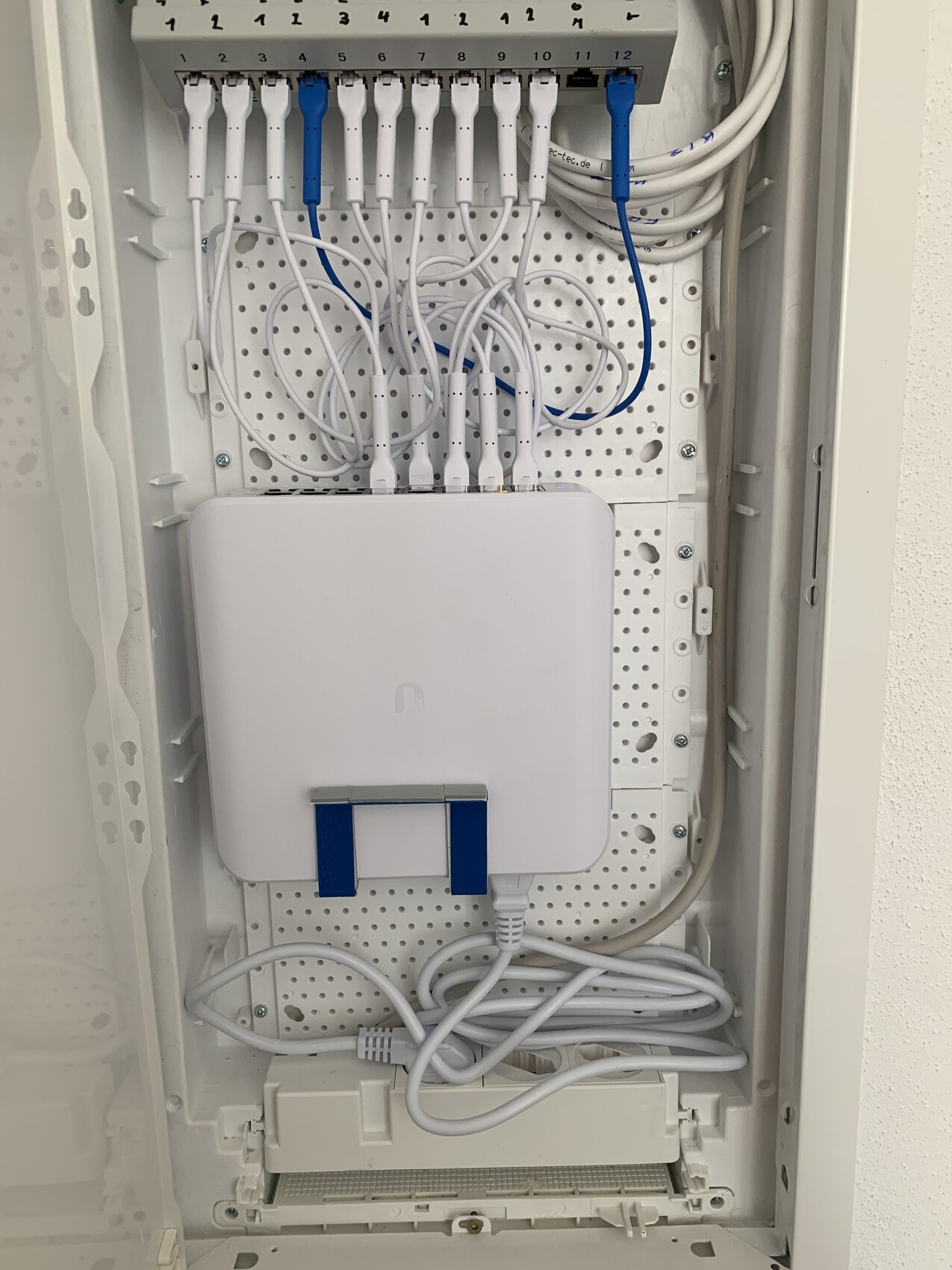 Netzwerk-Schrank: Patchpanel mit vielen weißen Kabeln, zwei blauen Kabeln, weiße Box unten