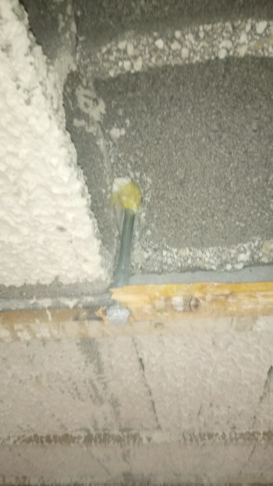 Gelbgrünes Rohr ragt aus rauer Wand im Rohbau, umgeben von Putz und Holzresten.