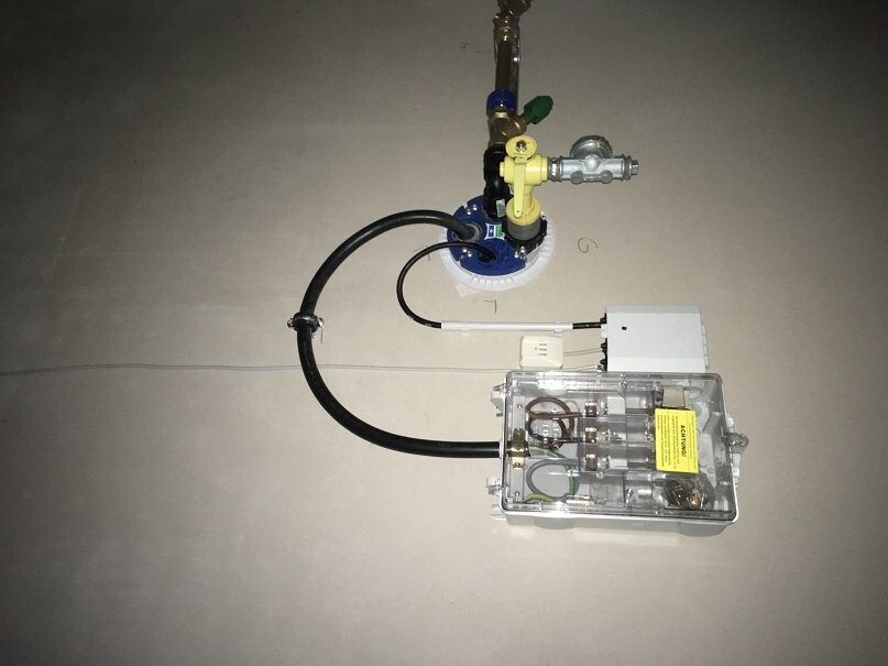 Haustechnik-Installationskomponenten: Gasventil, Schläuche und Elektronik auf Bodenplatte.