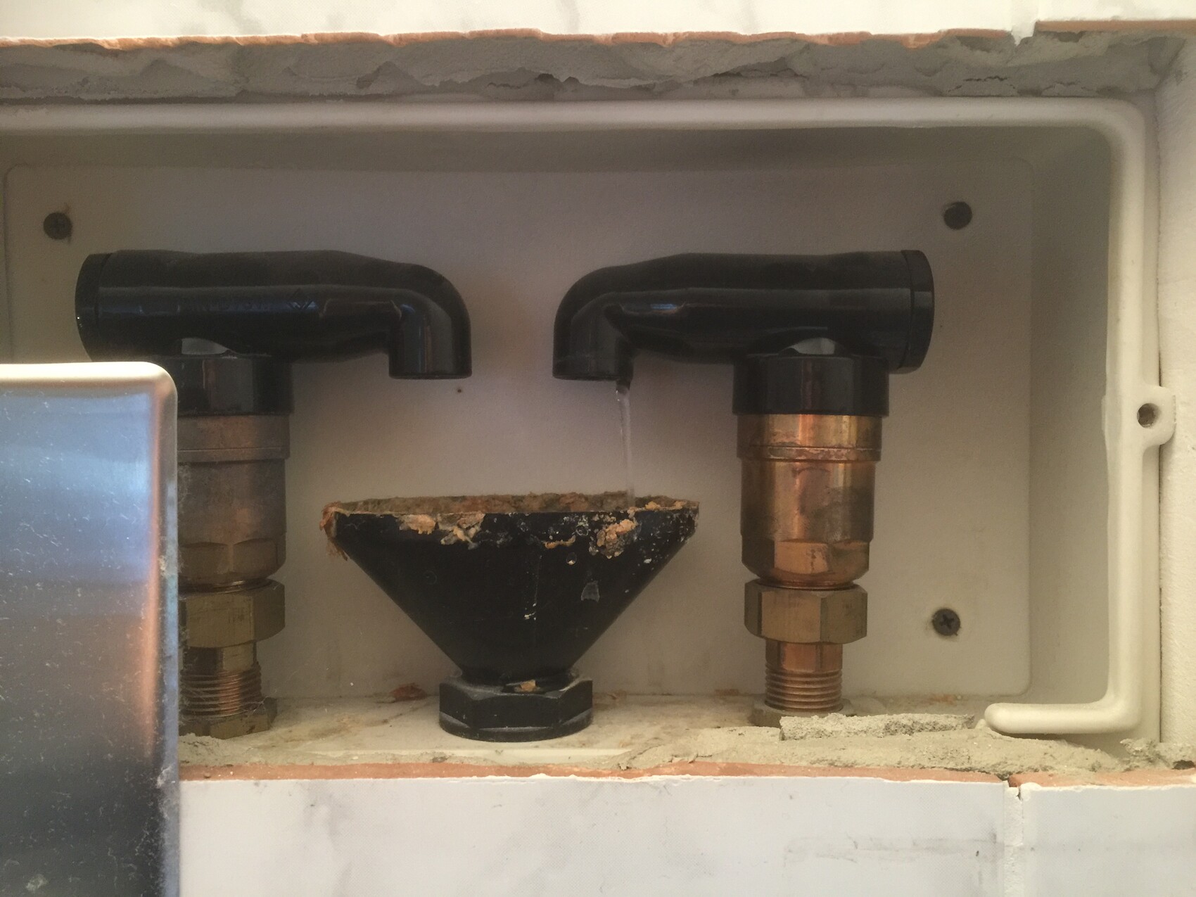 Unterputz-Wasserleitungen: zwei schwarze Rohrbögen verbinden Kupferleitungen; mittig ein Trichter.