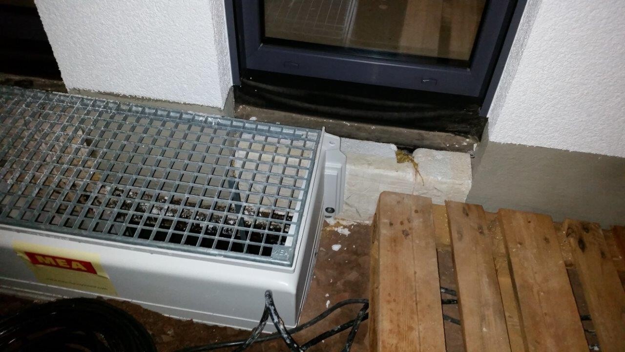 Metallgerät mit Gitternetz steht neben Tür; Holzbretter und Kabel liegen auf dem Boden.
