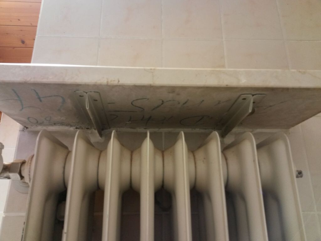 Badezimmer Heizkoerper mit Rippen vor Fliesenwand, seitlich montiert