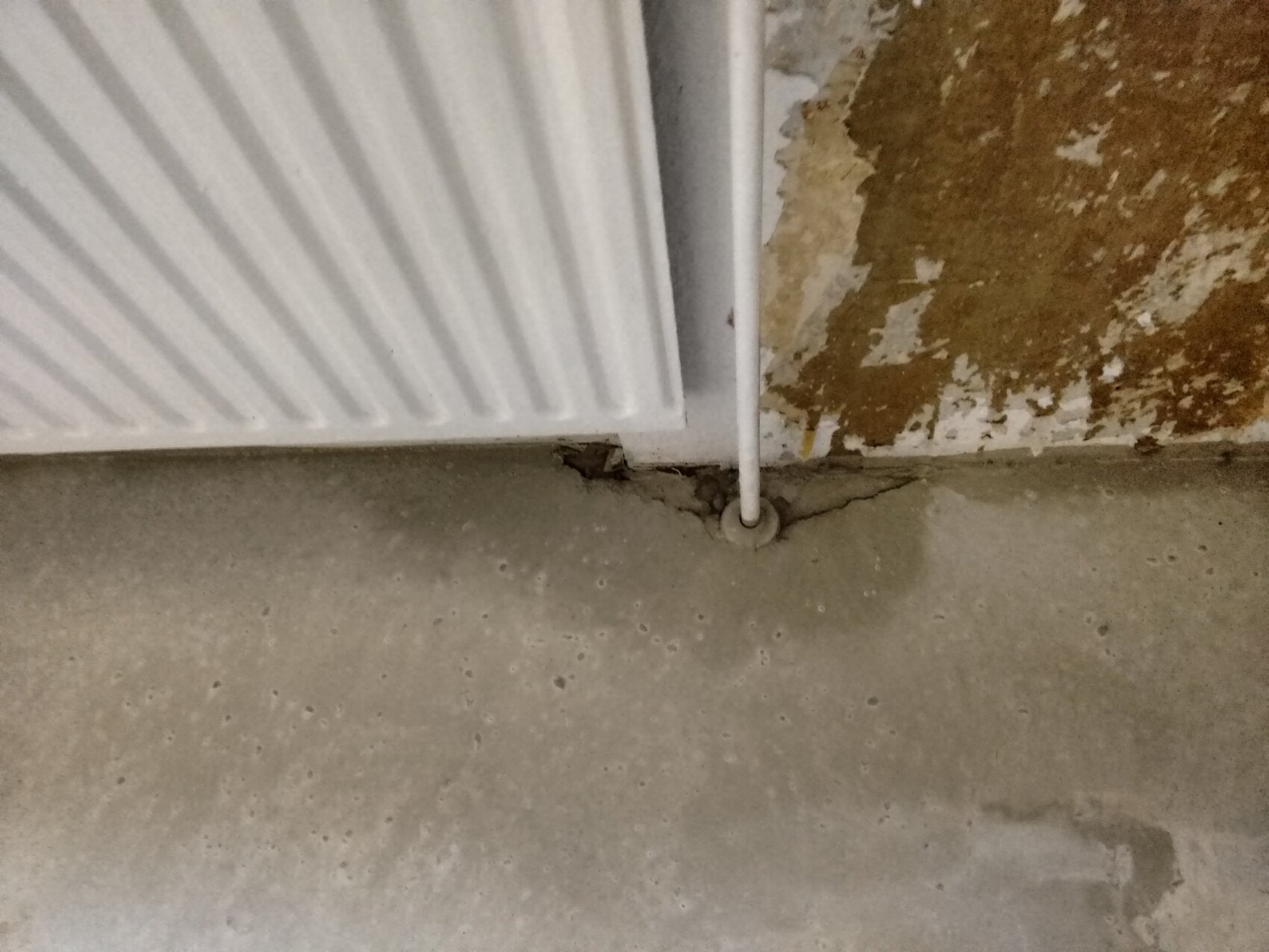 Weisser Heizkoerper im Keller, Wandriss und Bodenrisse im Betonboden