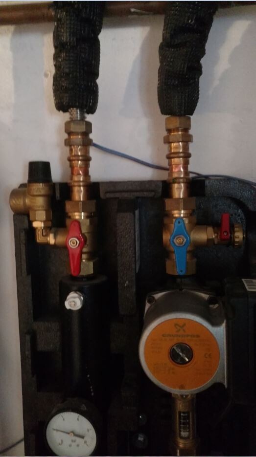 Heizungsverteiler mit zwei Ventilen (rot/blau), Grundfos-Pumpe und Druckmesser aus Kupferrohren.