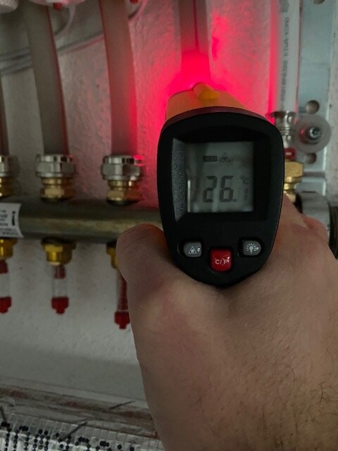 Hand hält Infrarot-Thermometer an Heizungsrohr; rotes Licht, Display zeigt ca. 26°C.