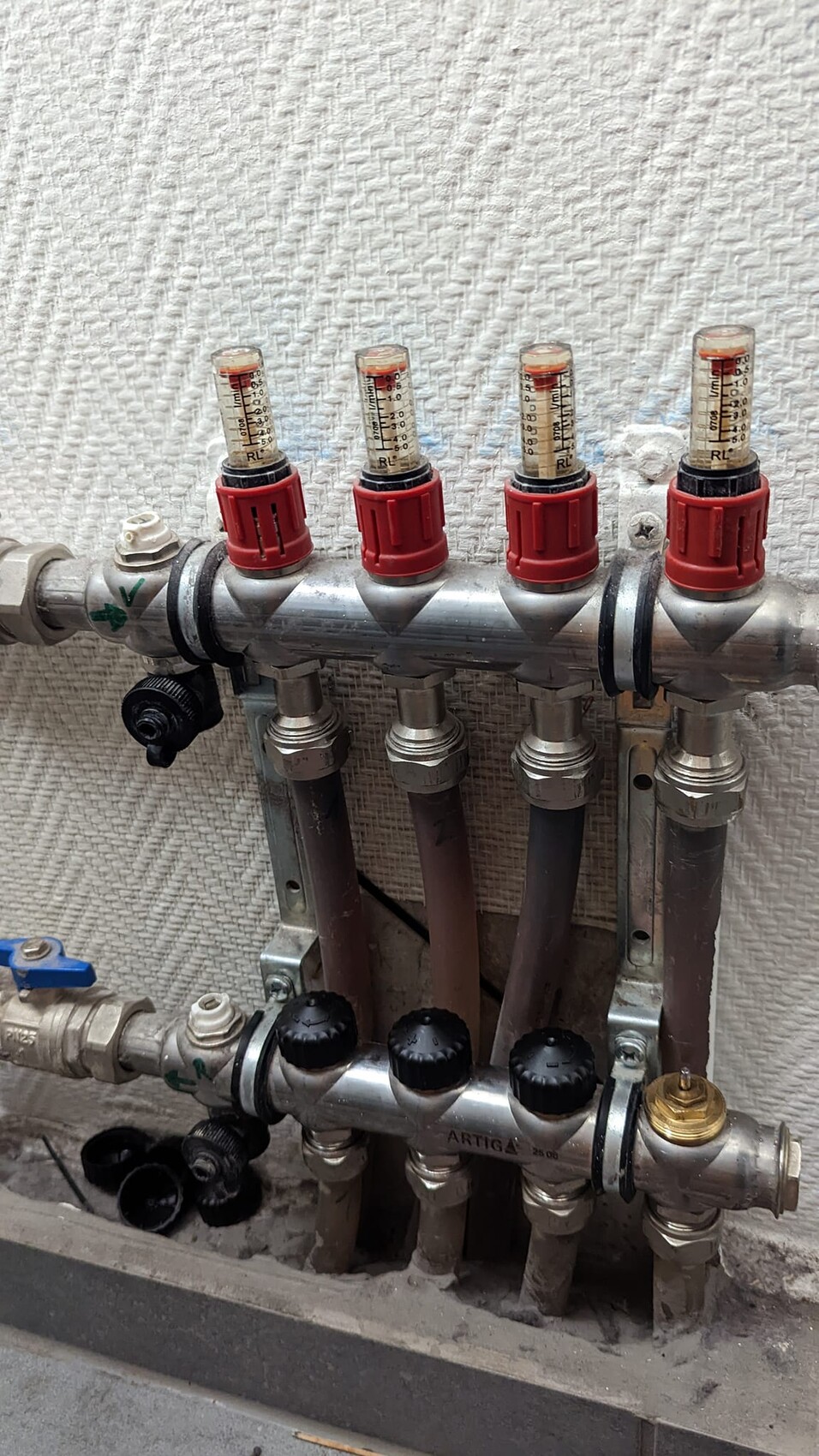 Heizungs-Verteiler mit vier roten Thermostatventil-Kappen, Rohren und Anschlüssen.