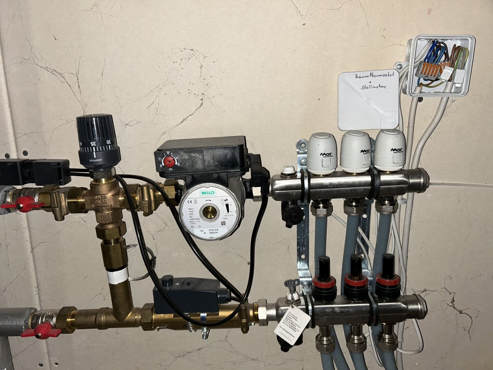 Haustechnikraum mit Heizungsverteiler, Pumpe, Ventile und Elektroanschluss an der Wand.