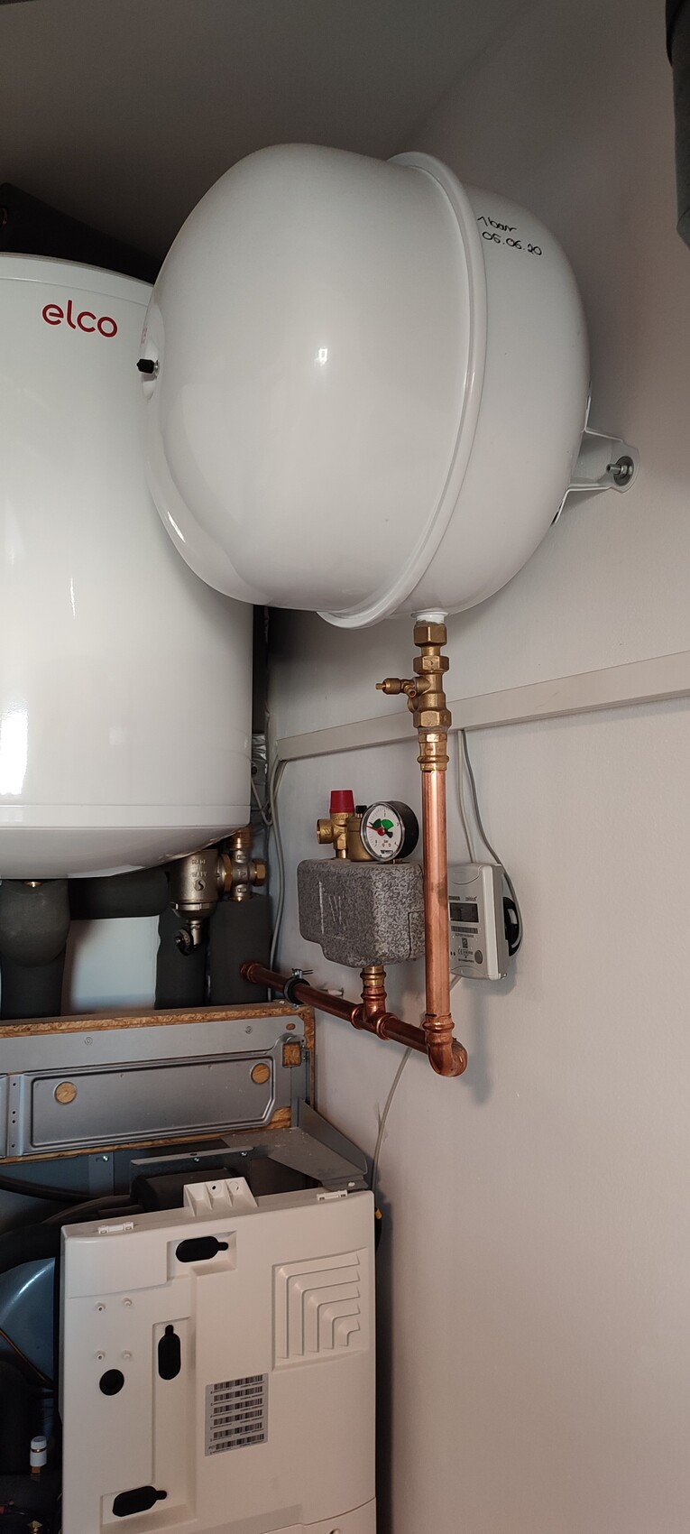 Heizungsraum mit Warmwasserkessel, Ausdehnungsgefäß, Druckmessgerät und Kupferrohrinstallation.