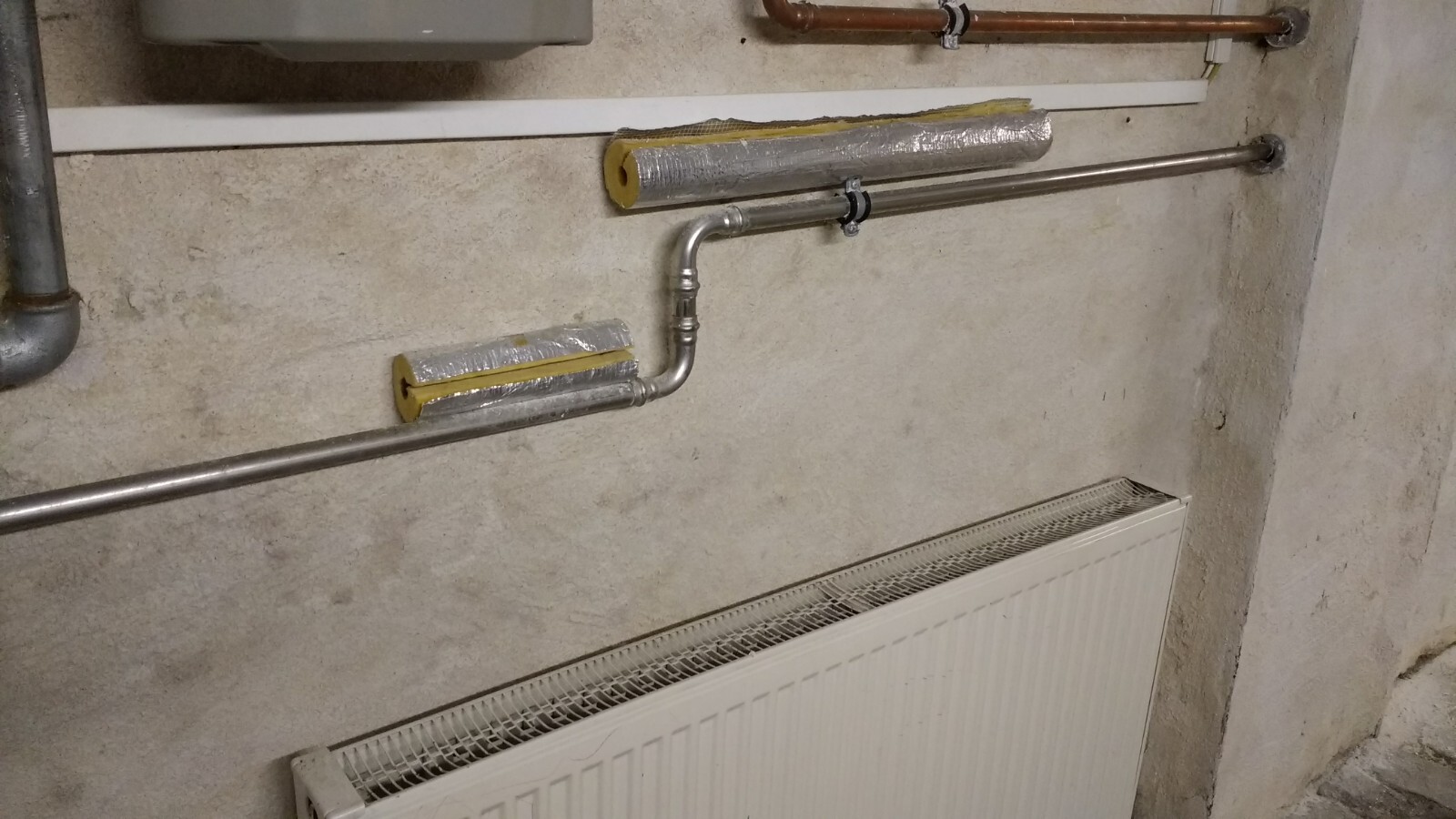 Kellerwand mit Heizungsrohren, Isolierung und Heizkörper
