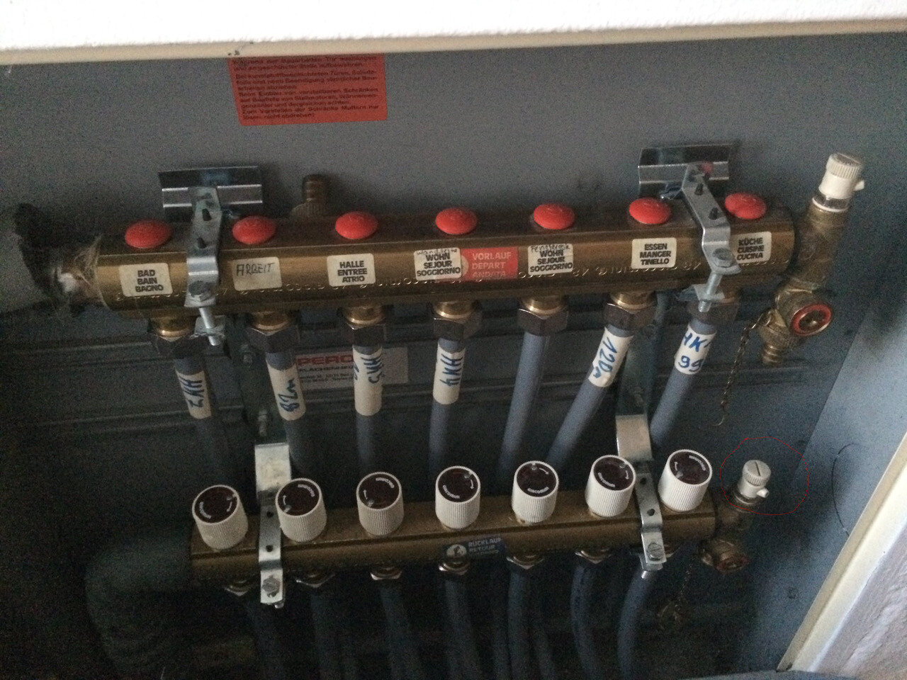 Hydraulischer Heizungsverteiler mit roten Deckeln, blauen Schläuchen und vielen Anschlüssen.