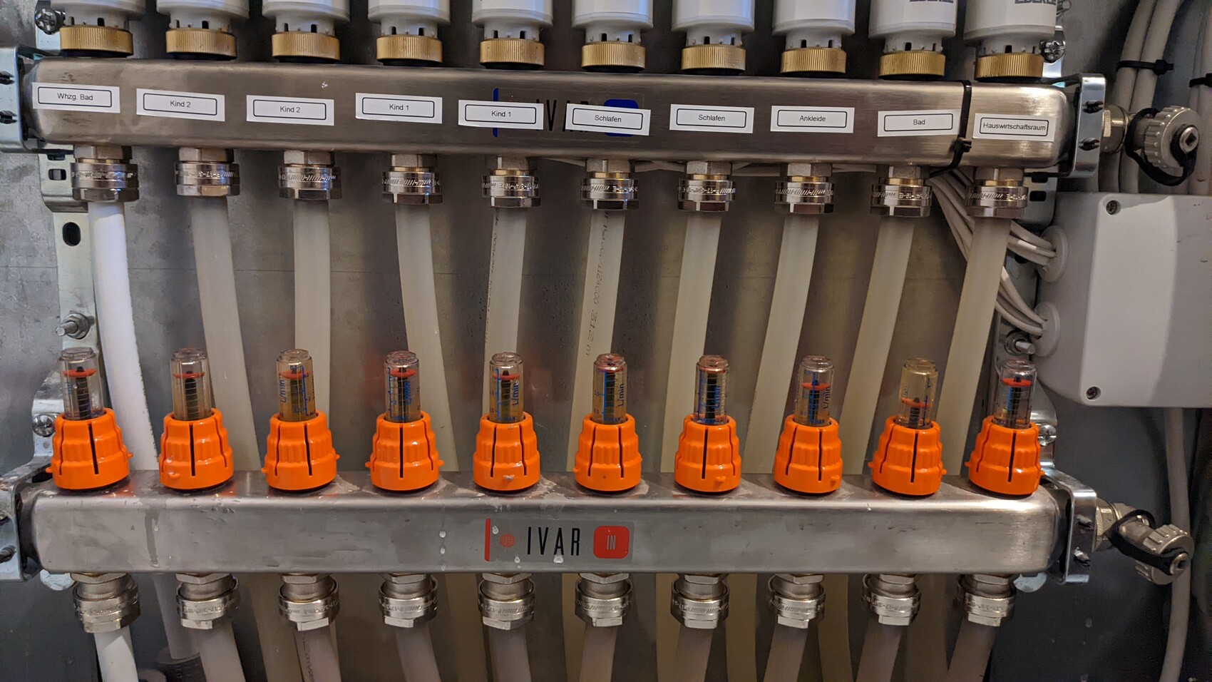Metallische Verteilerleiste mit vielen transparenten Röhrchen und orange Kappen.